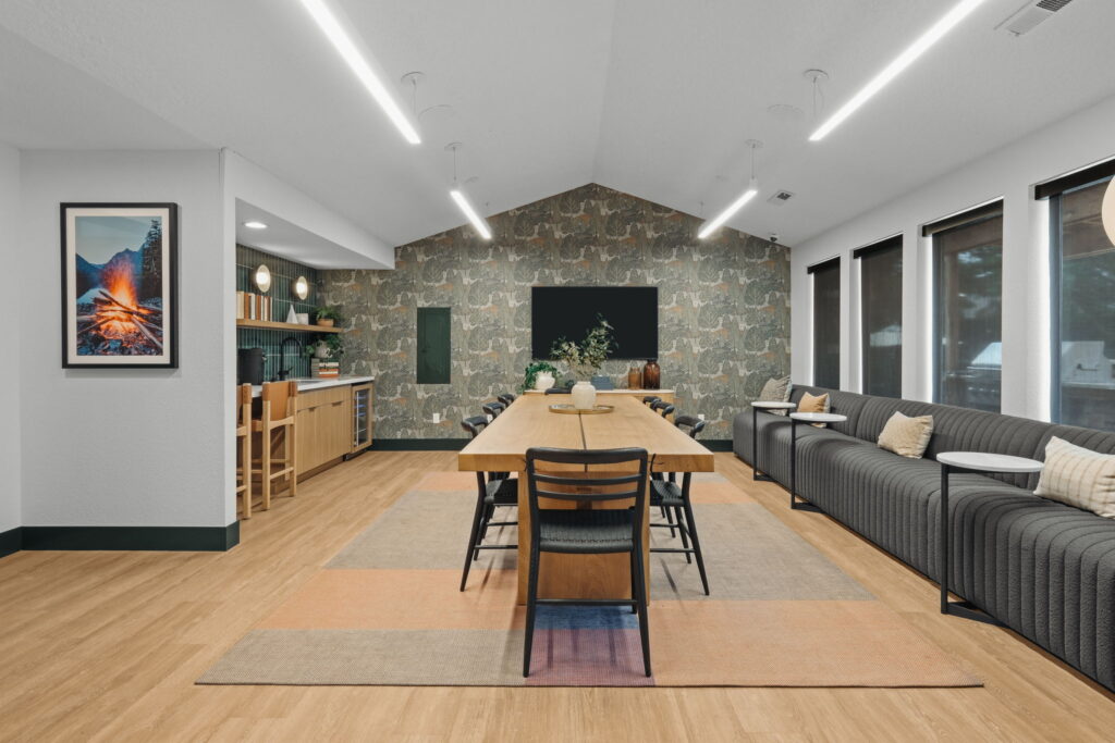 Spacious leasing office dining area with a long wooden table, black chairs, and a patterned accent wall. Cozy couch with pillows and large windows.