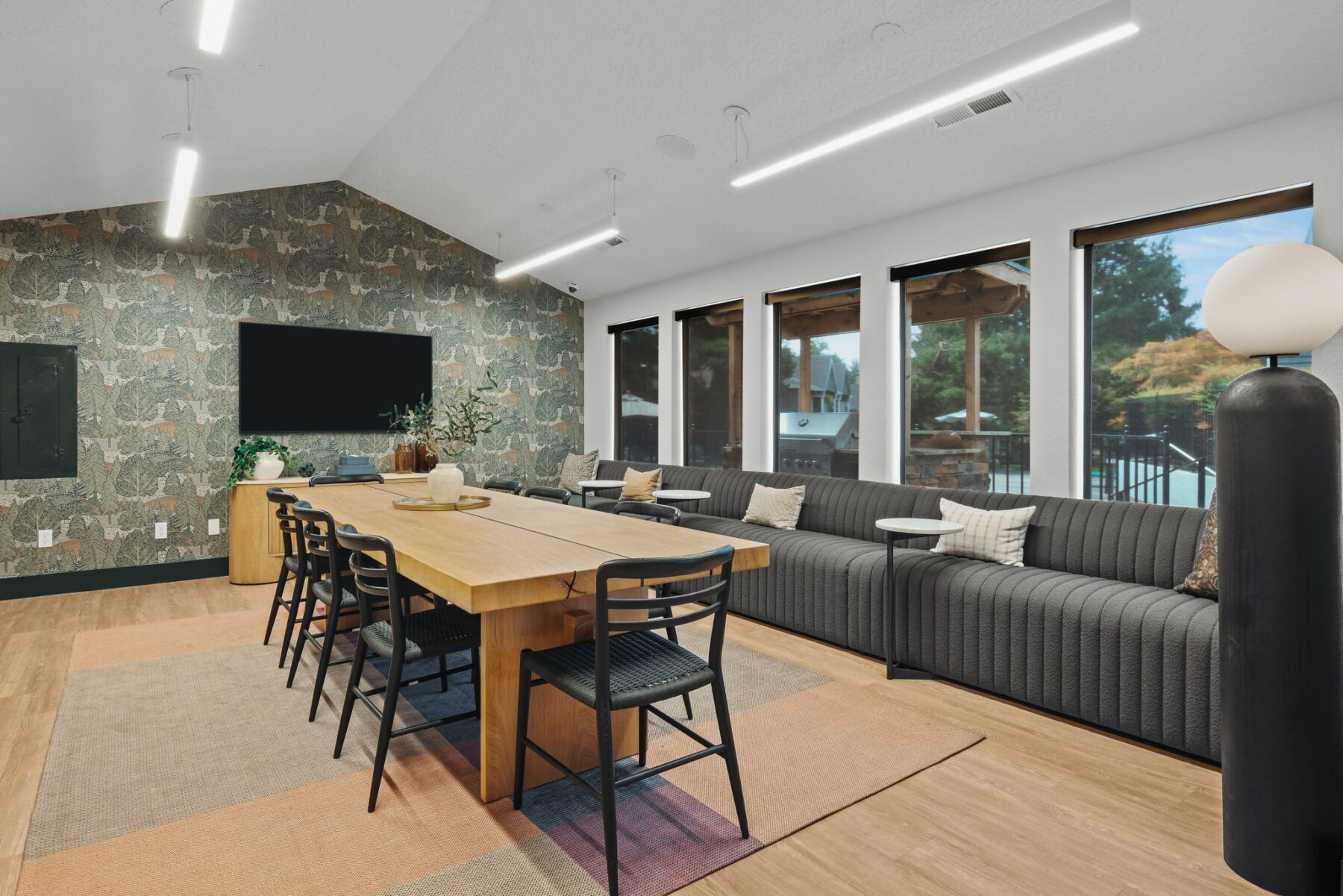 Spacious leasing office dining area with a long wooden table, black chairs, and a patterned accent wall. Cozy couch with pillows and large windows.