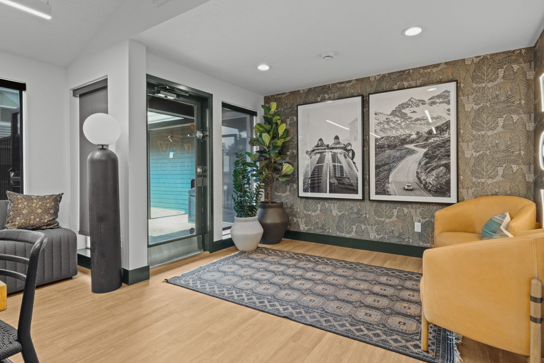 Stylish leasing office entry with modern decor. Features a tan armchair, large gray lamp, two black and white photographs, and plants.
