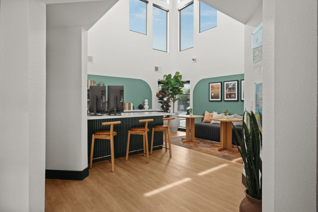 Modern leasing office with tall windows, light wooden floors, and green accents. Features a bar with wooden stools, seating, and lush plants.